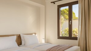 Una cama doble con sábanas blancas y un cabecero de madera, una ventana con vistas a árboles y una cortina a la derecha.