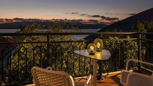 Un balcón con una mesa y dos sillas, con vistas a un paisaje pintoresco de un lago y montañas al atardecer.
