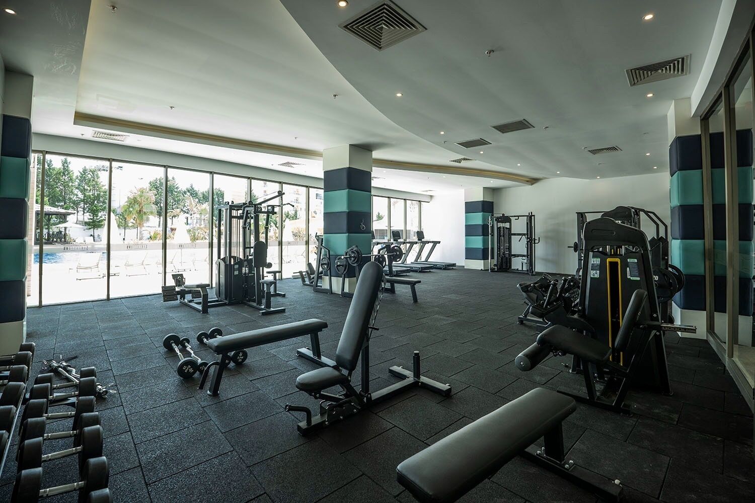 Ein Fitnessstudio mit verschiedenen Trainingsgeräten, großen Fenstern und Blick ins Freie.
