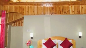 A wooden cabin-style room with a bed, two red pillows, a nightstand, a vase with flowers, and a wooden ceiling. - Home in the lap of nature 
In a peaceful location..... Darjeeling (WB)