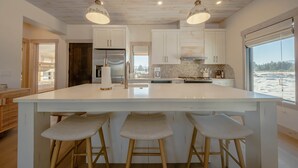 Una cocina moderna con una isla grande, armarios blancos y vista al mar.
