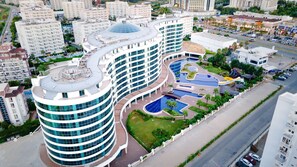 Een modern hotel met een gebogen gevel, meerdere verdiepingen en een centrale binnenplaats met zwembaden en groen.