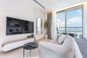 A modern living room with a flat-screen TV, a sofa, a small table, and a large window with a city view.