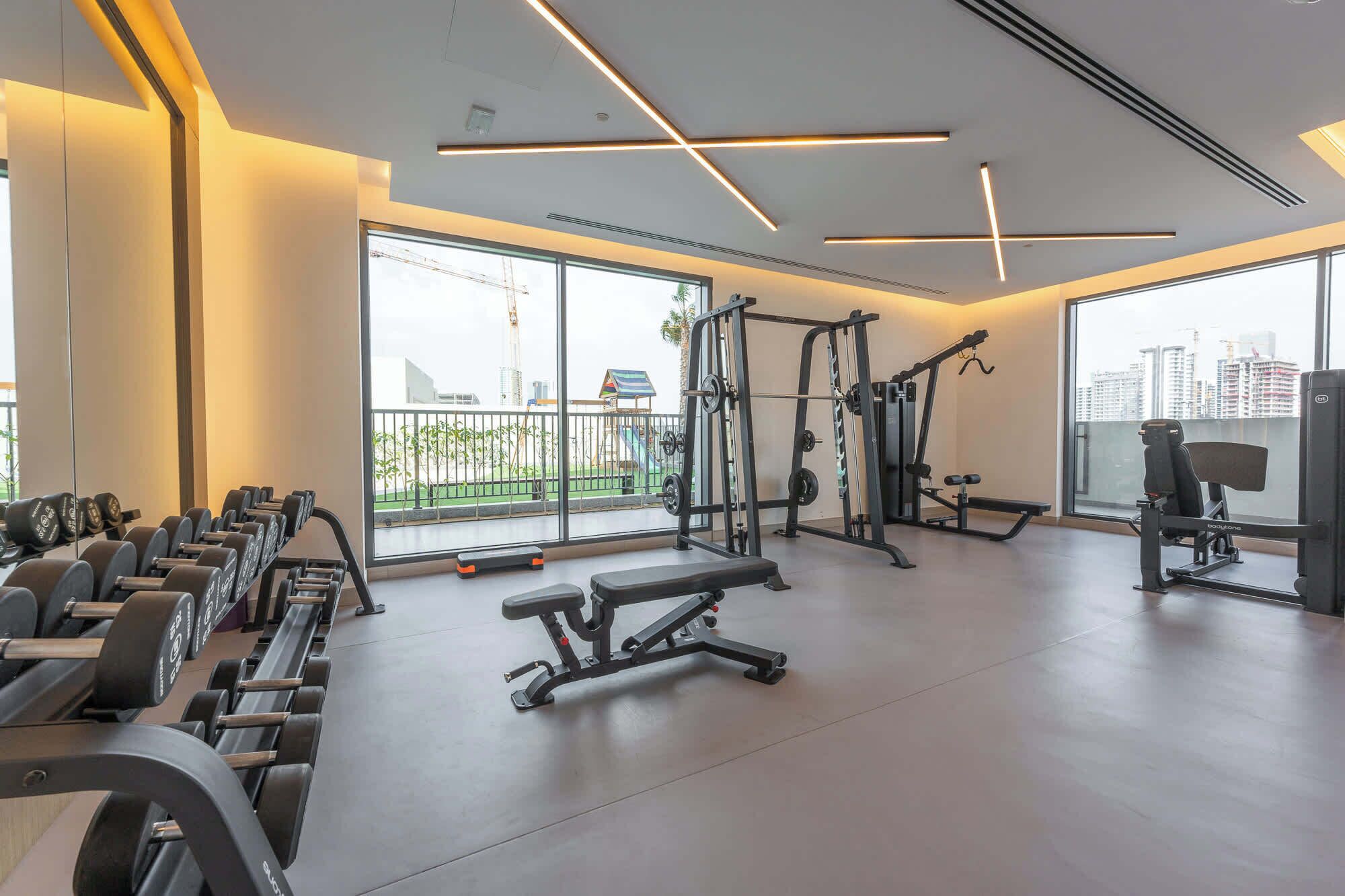 A modern gym with various exercise equipment, large windows, and a view of the cityscape.