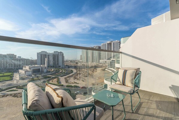 A balcony with a view of a cityscape, including high-rise buildings and a road. There are two chairs and a small table.