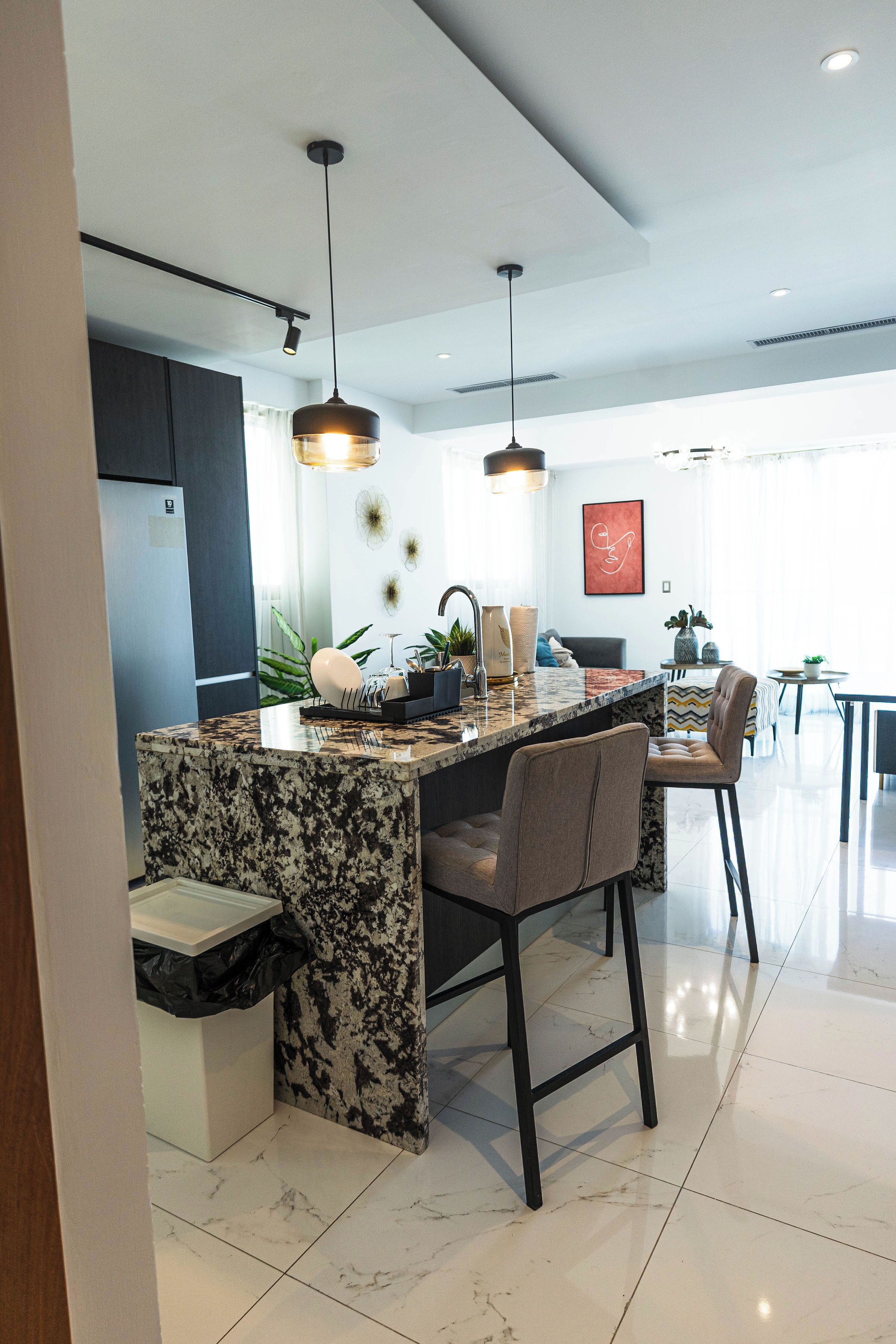 A modern kitchen with a granite island, pendant lighting, and a dining area with chairs.