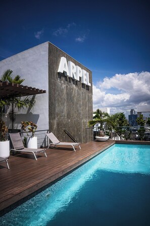 Un edificio moderno con el nombre 'ARPEL' en su fachada, una piscina y sillones de descanso.