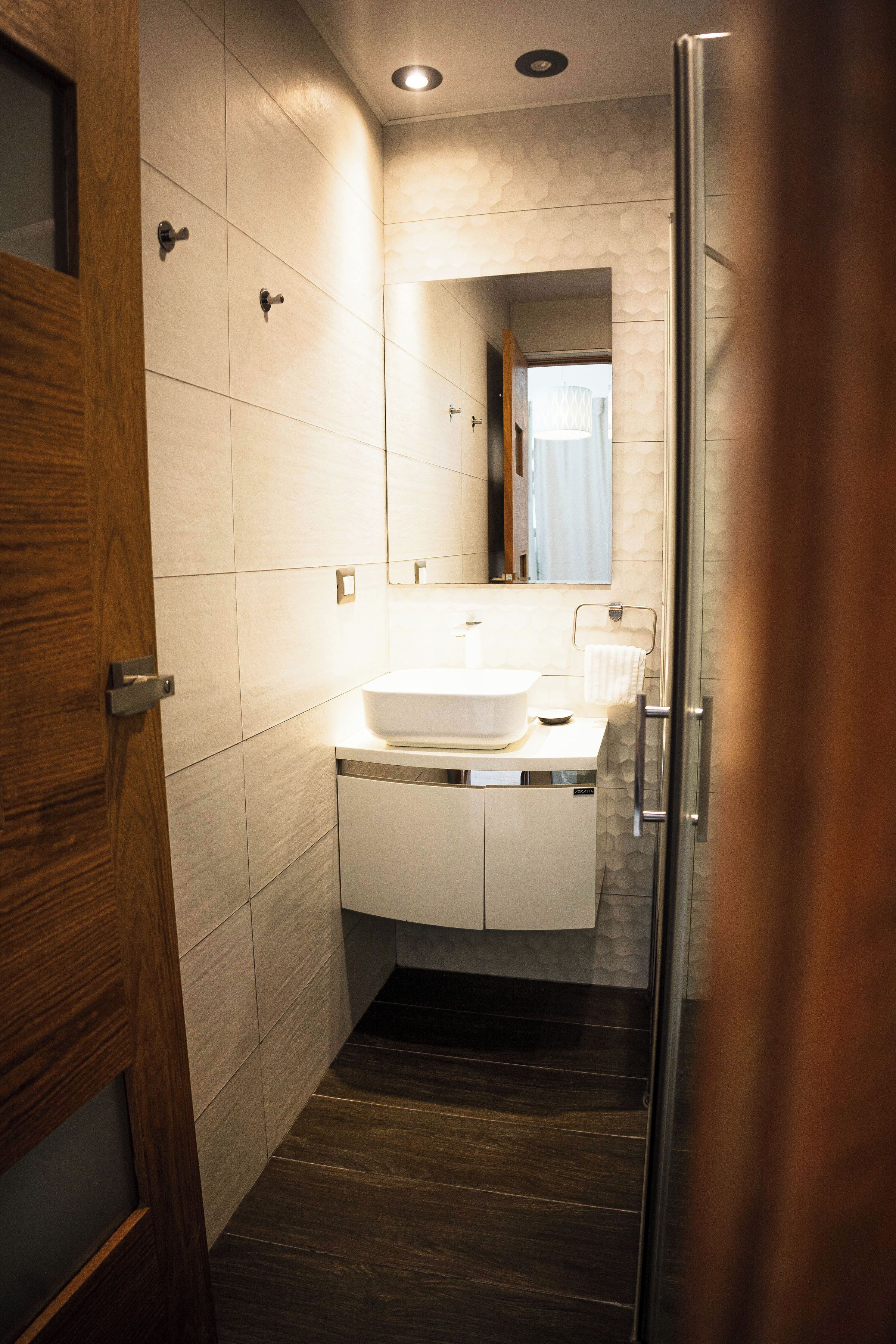 Een moderne badkamer met een houten deur, een witte wastafel met een spiegel erboven en een douchecabine van glas.