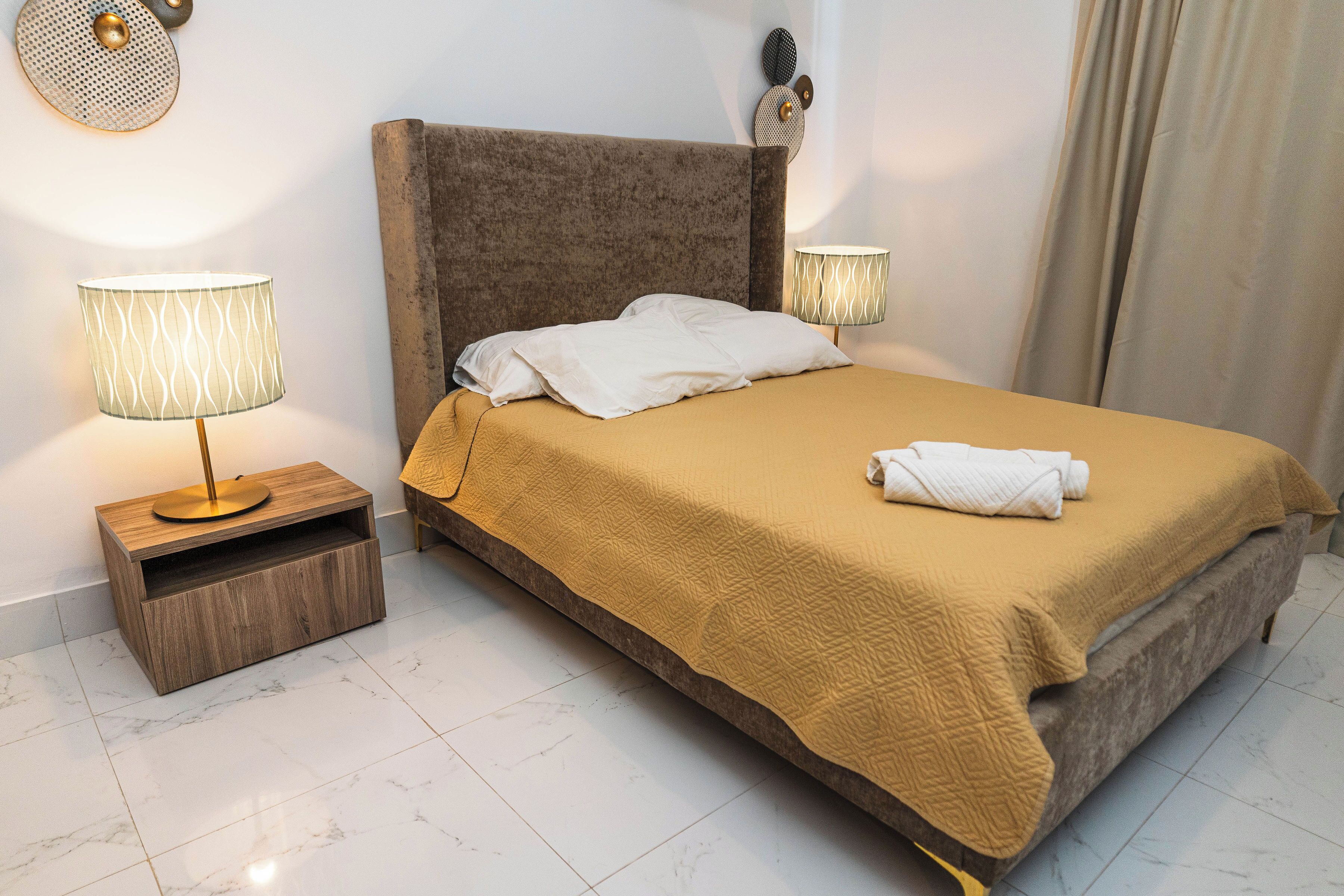 A neatly made bed with a brown headboard, two bedside lamps, and a wooden nightstand.