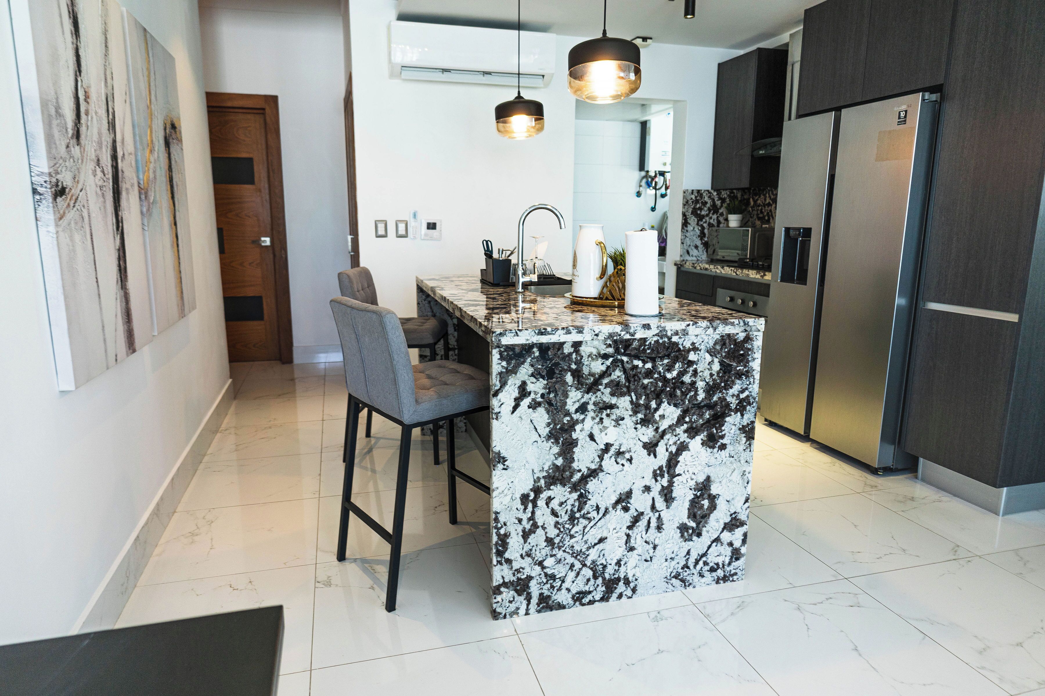 Een moderne keuken met een marmeren eiland, donkere kastjes en roestvrijstalen apparatuur.