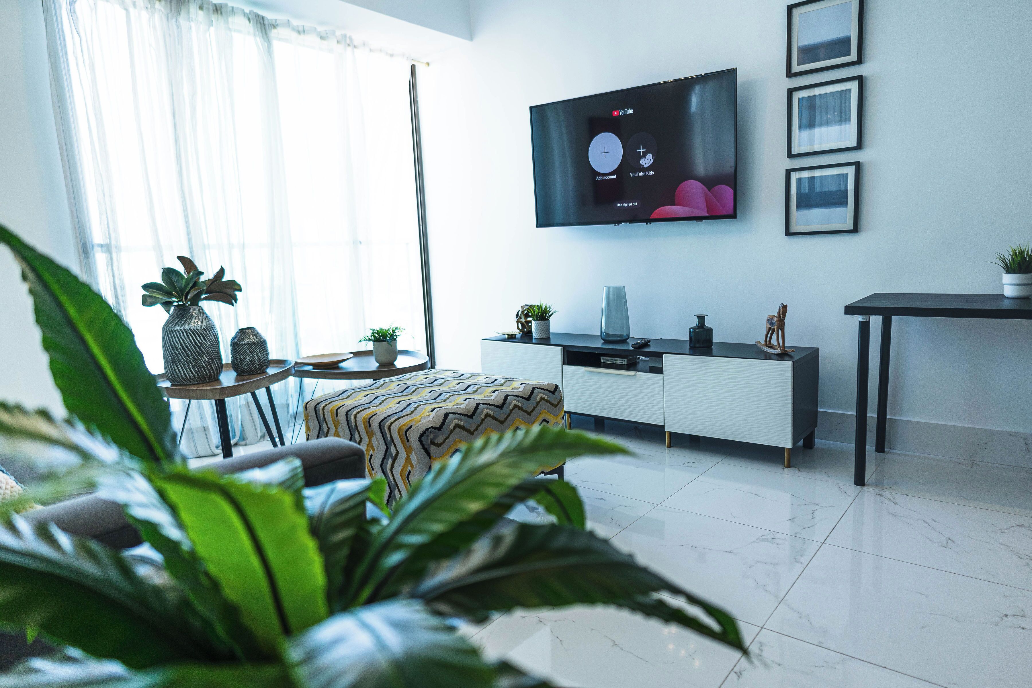 A modern living room with a flat-screen TV mounted on the wall, a sofa, a coffee table, and a dining area with a table and chairs.
