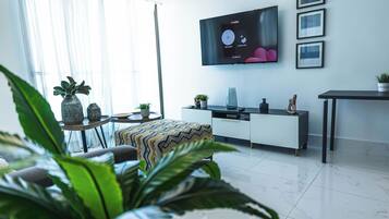 A modern living room with a flat-screen TV mounted on the wall, a sofa, a coffee table, and a dining area with a table and chairs.