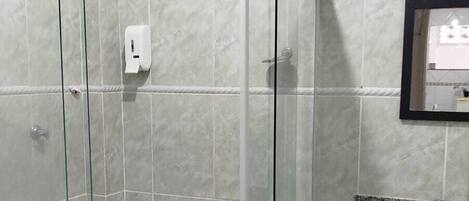 En duschkabin med en glasdörr, ett duschmunstycke som kan hållas i handen och en väggmonterad tvåldispenser.