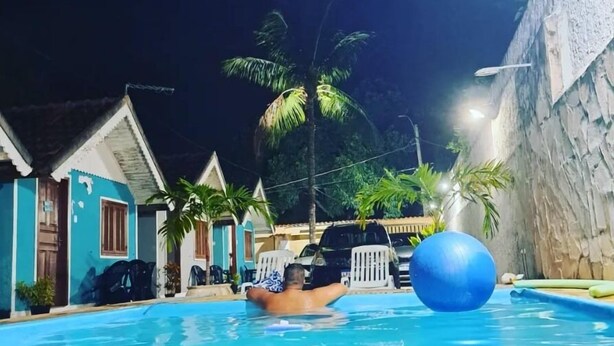 A swimming pool with a person floating, surrounded by houses and palm trees. - Pousada Do Sol (Rio de Janeiro)