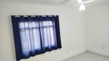 A room with a single window, white walls, and a ceiling fan.