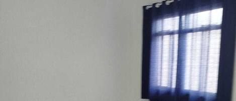 Huoneessa on kattotuuletin, ikkunassa verhot ja lattiassa laatat.