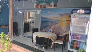 A restaurant with a table and chairs, a refrigerator, and a mural of a sunset. - Pousada Do Sol (Rio de Janeiro)
