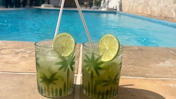 Two glasses of a green beverage with lime slices on a poolside table.