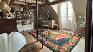 Un espacioso dormitorio tipo loft con una escalera de madera, un tapete floral grande y un sofá blanco.