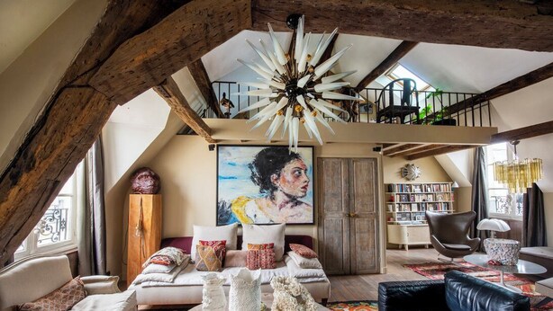 Un loft espacioso con vigas de madera a la vista, un ventilador de techo grande, un cuadro, una estantería y una zona de estar acogedora con un sofá y sillones de cuero.