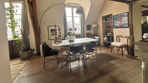 Un comedor con una mesa y sillas, una ventana con cortinas y una estantería con diversos objetos.