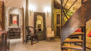 A rustic interior with a stone wall, a wooden chair, a white armchair, a mirror, and a spiral staircase. - 18TH-CENTURY PALACE, BLEND OF OLD-WORLD GRANDEUR & MODERN COMFORT - LE MARAIS (Paris)