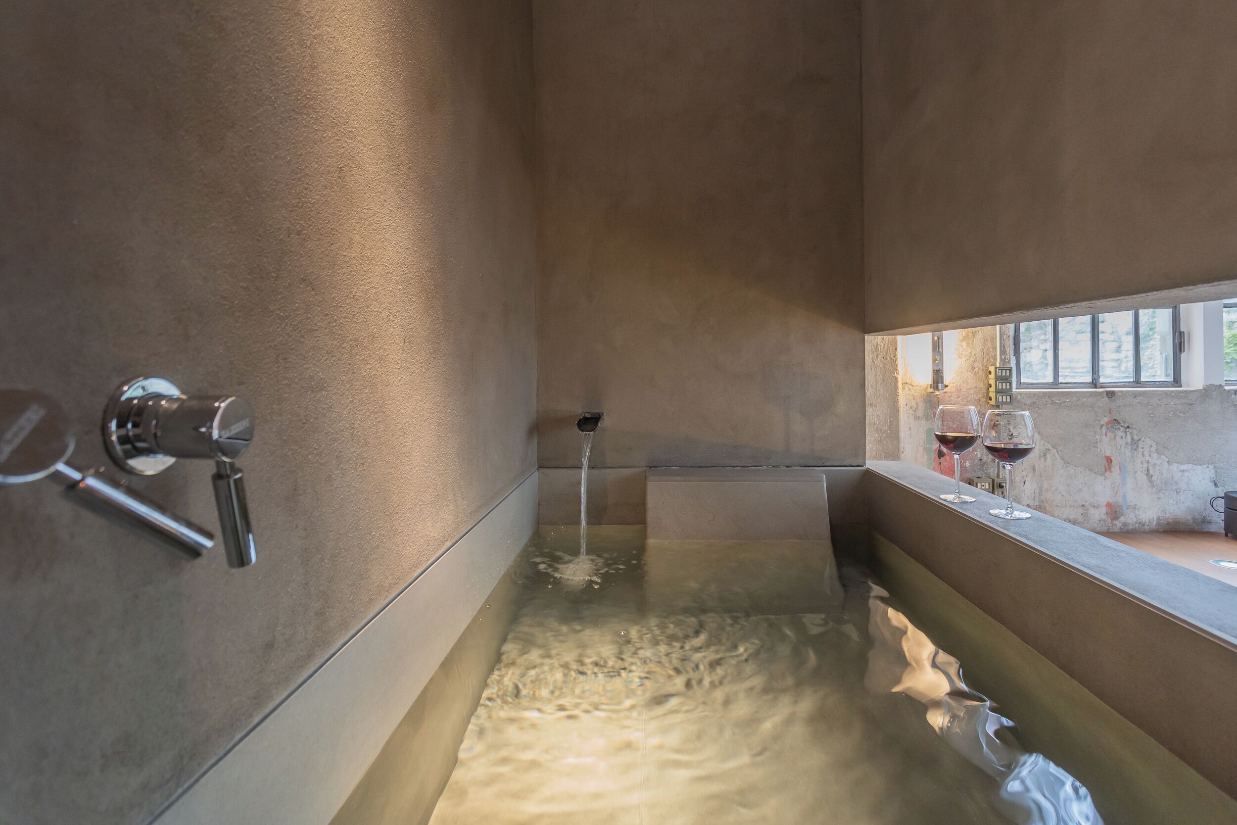 Ein modernes Badezimmer mit einer Badewanne, einem Wasserhahn und einem Fenster mit zwei Weingläsern.