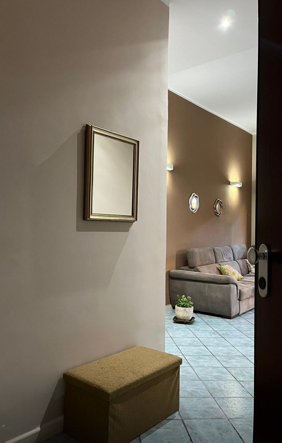 Ein modernes Wohnzimmer mit einer Couch, einem gerahmten Bild an der Wand und einer kleinen Pflanze auf dem Boden.
