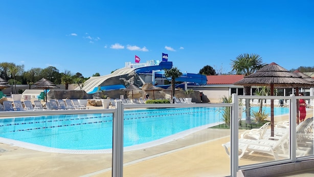 Una piscina con sillas de descanso, tobogán de agua y un pabellón.