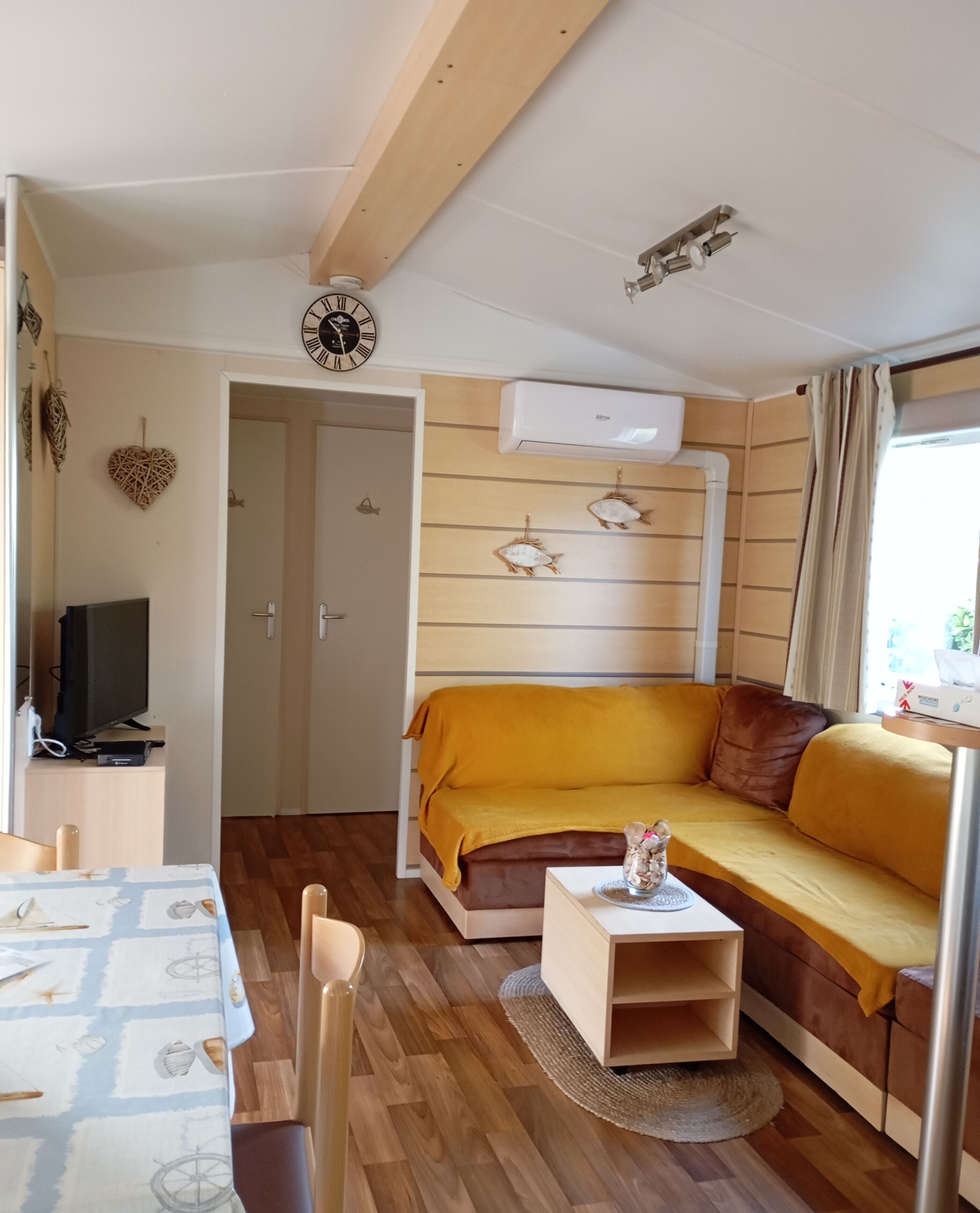 A compact living space with a sofa, a small table, a TV, and a wall-mounted clock.