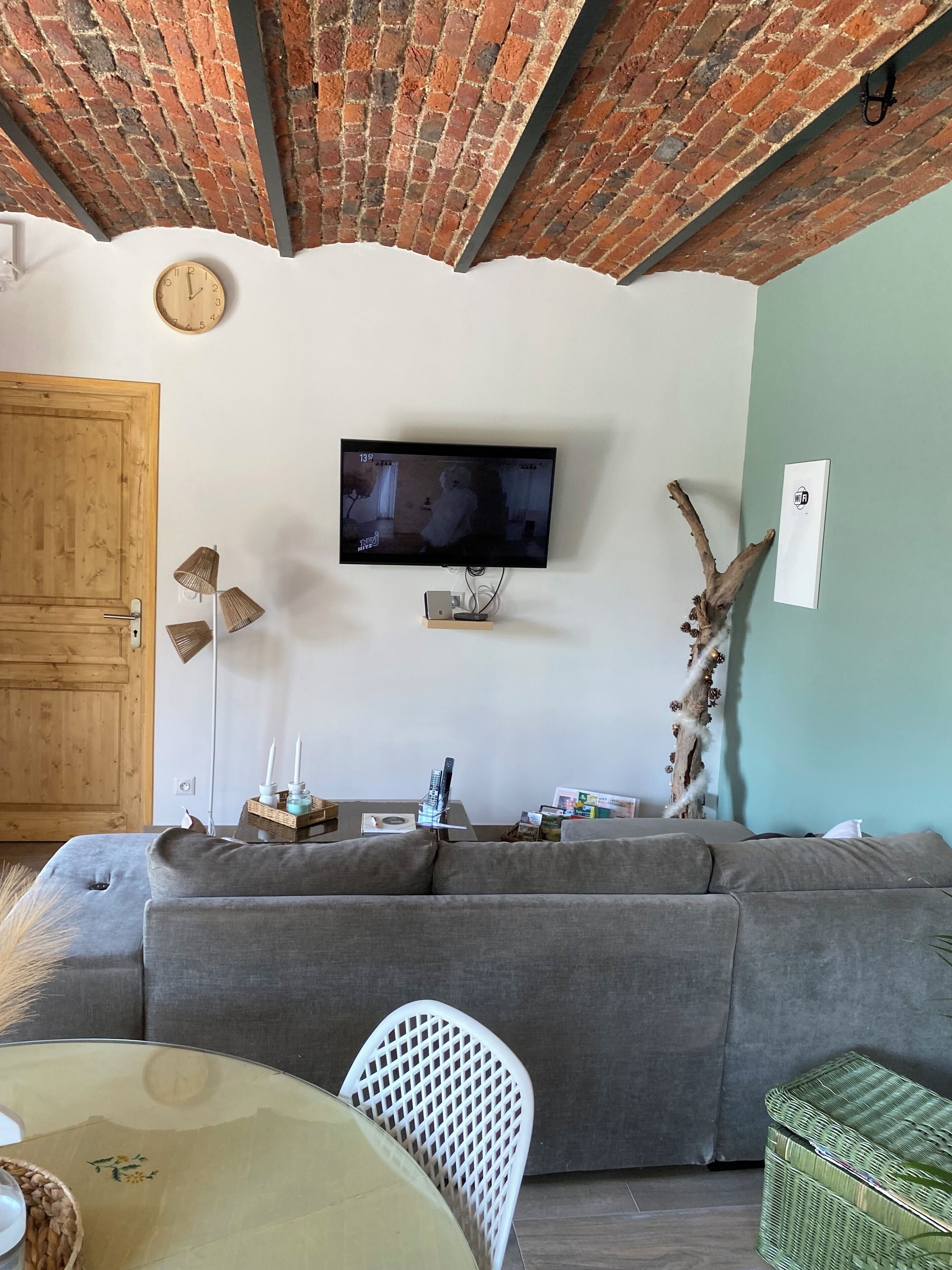 Una sala de estar acogedora con un sofá gris, un televisor montado en la pared, una puerta de madera y un techo de ladrillo.