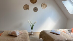 Ein Zimmer mit zwei Betten, einem an der Wand befestigten Haken für Hüte, einer Vase mit weißen Blumen und einem Oberlicht.