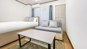 Ett hotellrum med en säng, en soffa, ett litet bord, en luftkonditioneringsanläggning och ett fönster med gardiner.