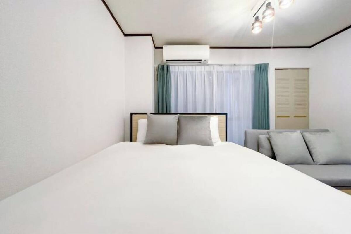 Una habitación de hotel moderna con cama, sofá, ventana con cortinas, unidad de aire acondicionado y lámpara.