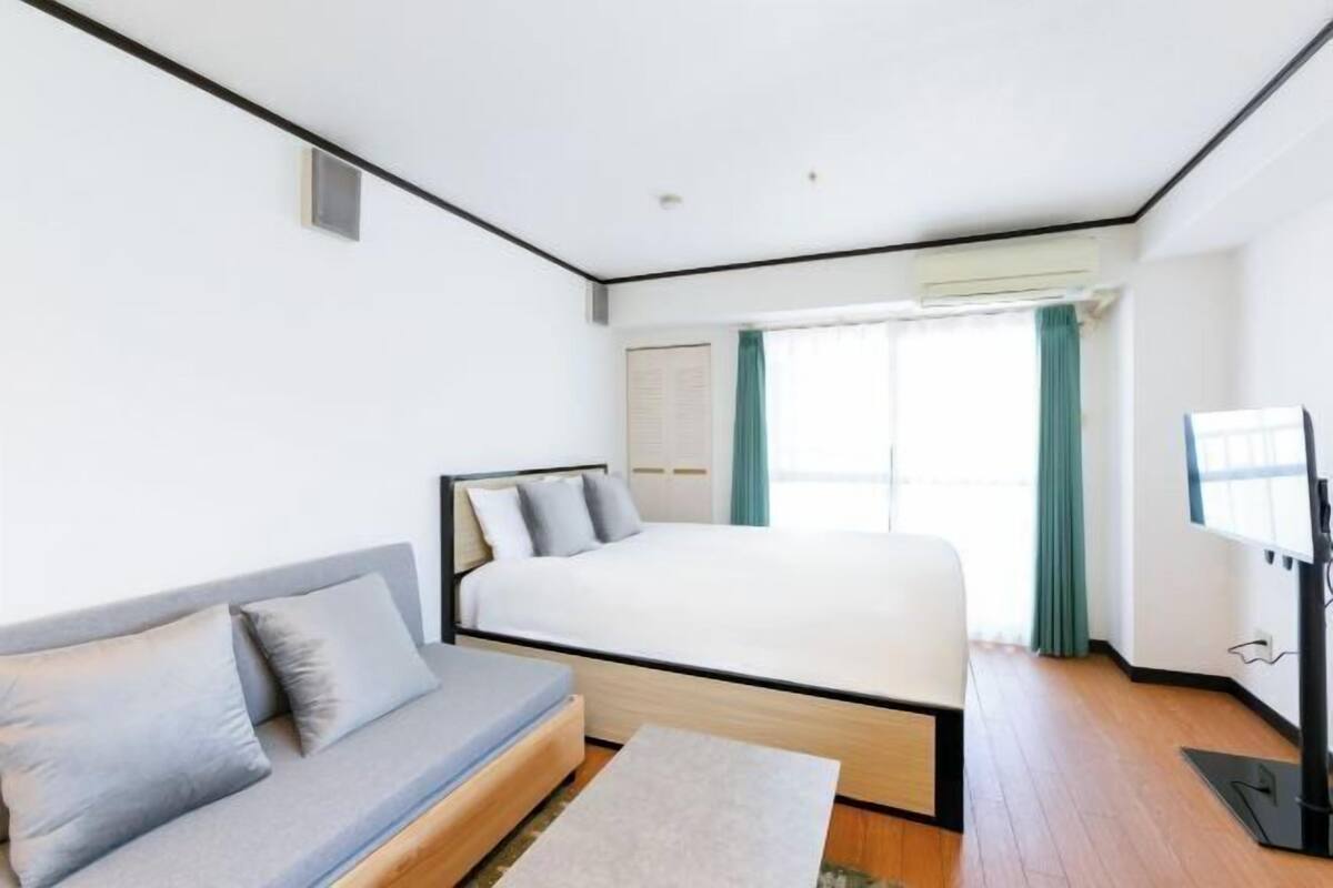 Un dormitorio con cama, sofá, televisión y ventana con cortinas.