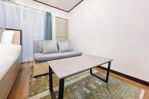 Une petite chambre moderne, équipée d’un lit, d’un canapé, d’une petite table et d’un tapis à motifs.