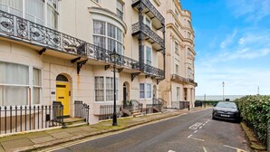 A row of traditional terraced houses with balconies, a clear road, and a parked car. - Coastal Breeze With Seaview By My Getaways (Brighton)