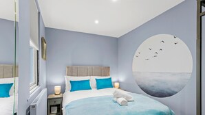 A bedroom with a bed, a nightstand, a wall mural, and a window. - Coastal Breeze With Seaview By My Getaways (Brighton)