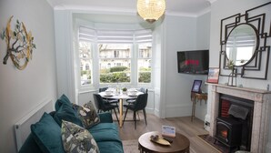 A living room with a sofa, a dining table, and a fireplace. - Coastal Breeze With Seaview By My Getaways (Brighton)