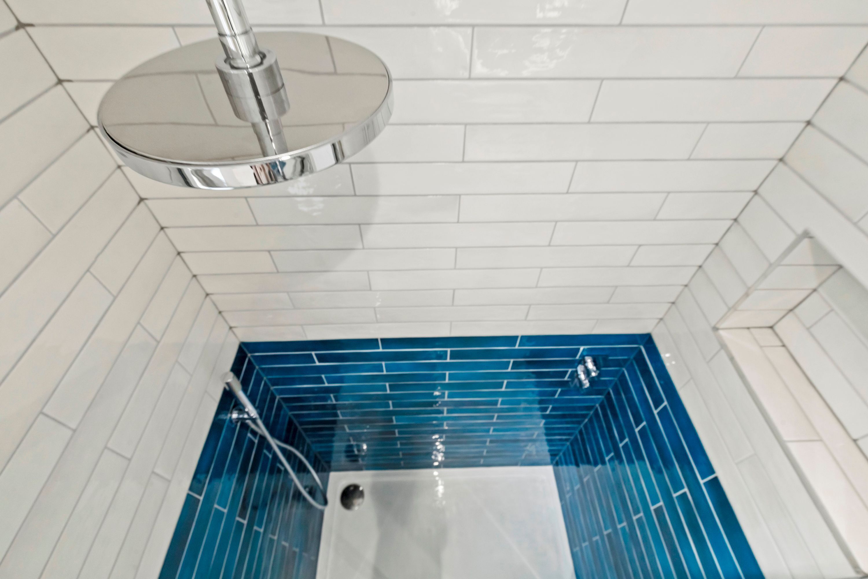 A bathroom with white tiled walls and a blue-tiled shower area.