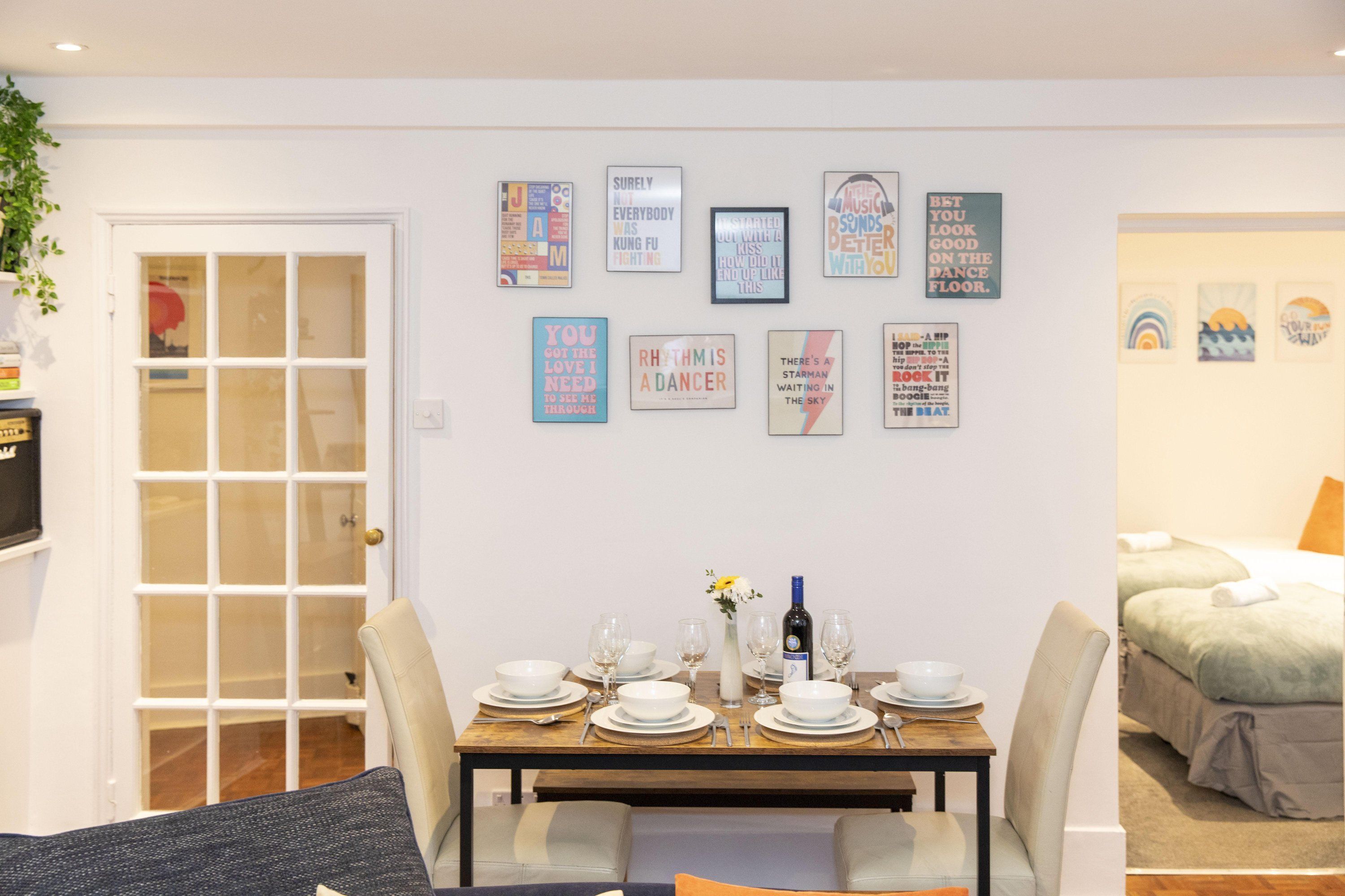 A dining area with a table set for four, a door with glass panels, and a bed with a green blanket.