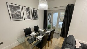 Spiseplads med et glasbord, sorte stole og billeder i rammer på væggen.