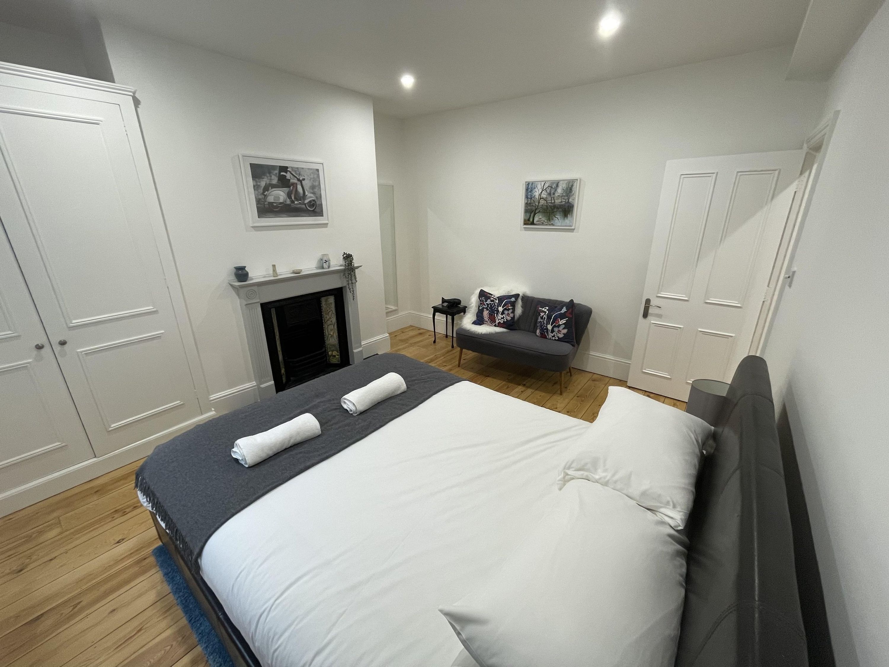 A modern bedroom with a large bed, a sofa, a fireplace, and a wardrobe.