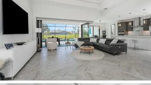 A modern living room with a large sectional sofa, a coffee table, and a flat-screen TV mounted on the wall.