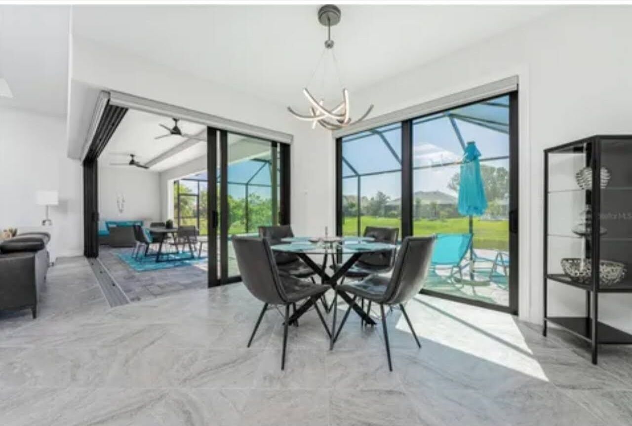 A modern dining area with a glass table and chairs, a ceiling fan, and a view of the outdoors.
