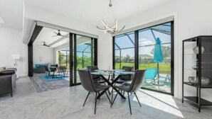 A modern dining area with a glass table and chairs, a ceiling fan, and a view of the outdoors.