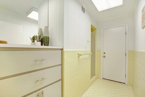 A bathroom with white walls, a yellow-tiled shower area, and a white door. - The Big Tybreezy (Tybee Island)