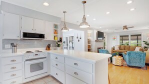 A modern kitchen with white cabinetry, a built-in oven, and a central island. - The Big Tybreezy (Tybee Island)