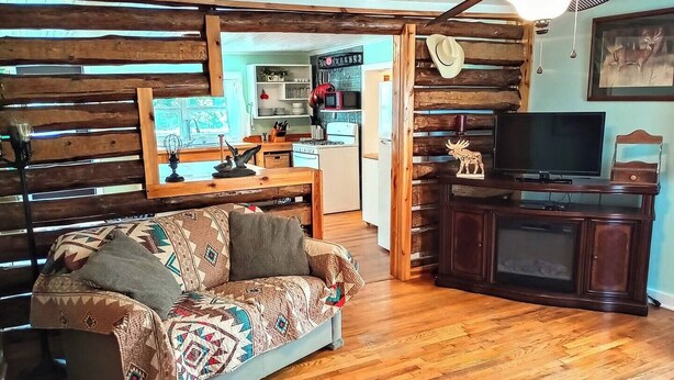 A cozy living room with a wooden sofa, a television on a wooden cabinet, and a ceiling fan. - Beula 1869 cabin in "The Land" (Calico Rock)