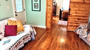 A cozy room with a wooden floor, a bed with patterned bedding, a door with a window, and a wooden wall. - Beula 1869 cabin in "The Land" (Calico Rock)